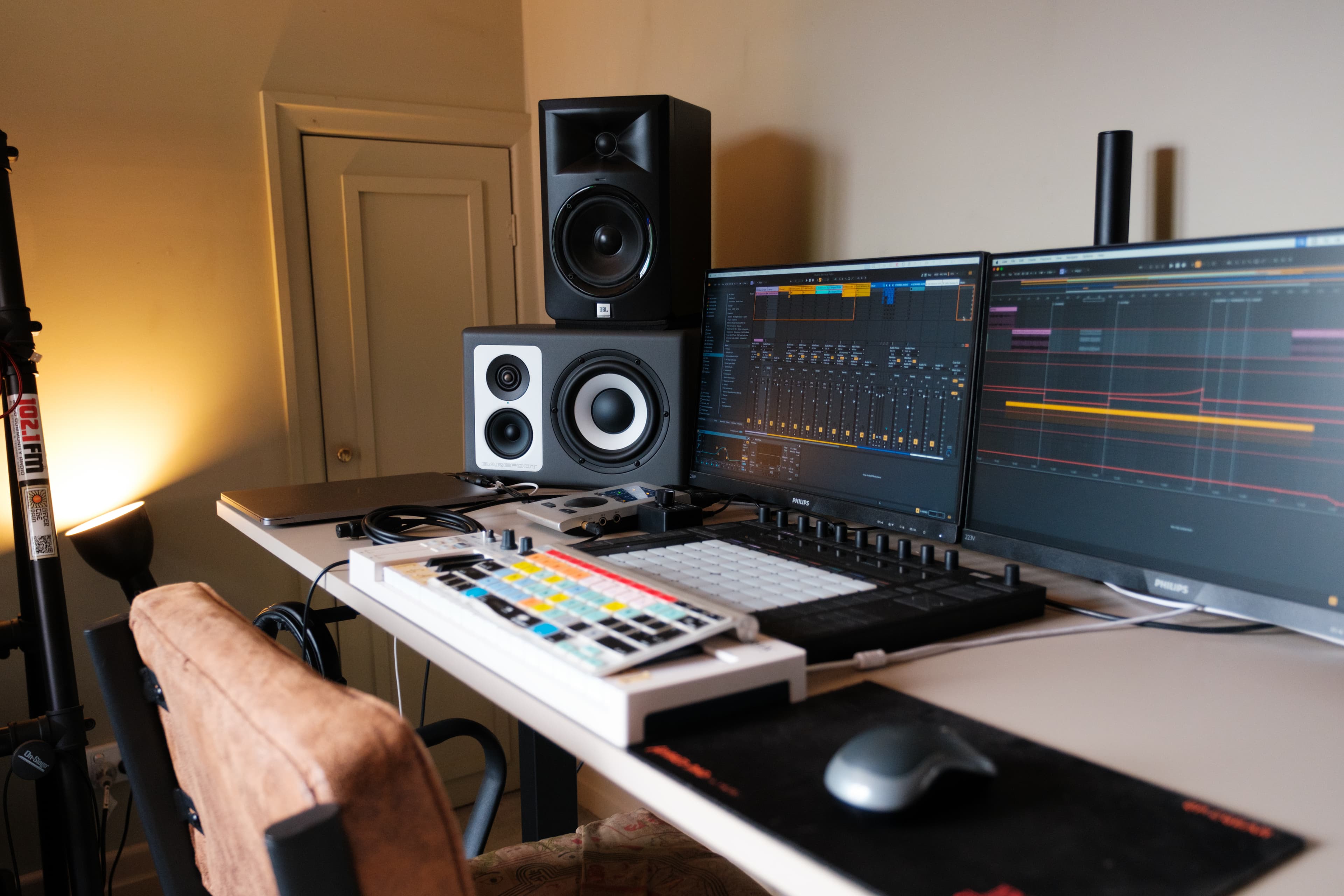 Studio desk with dual monitors running Ableton Live, a mixing controller, and a desk lamp